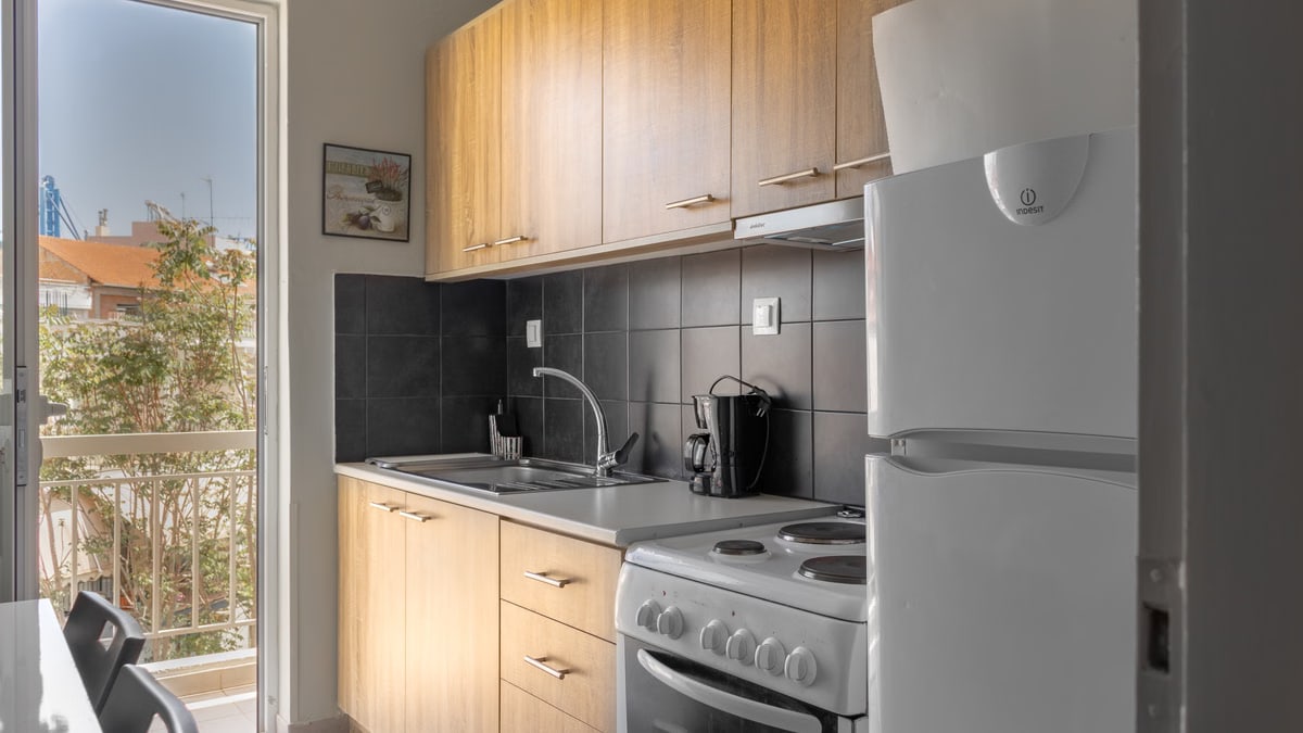 Sunny modern kitchen featuring wooden cabinets, appliances, and a balcony view.